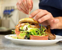 Person putting a skewer into a burger.